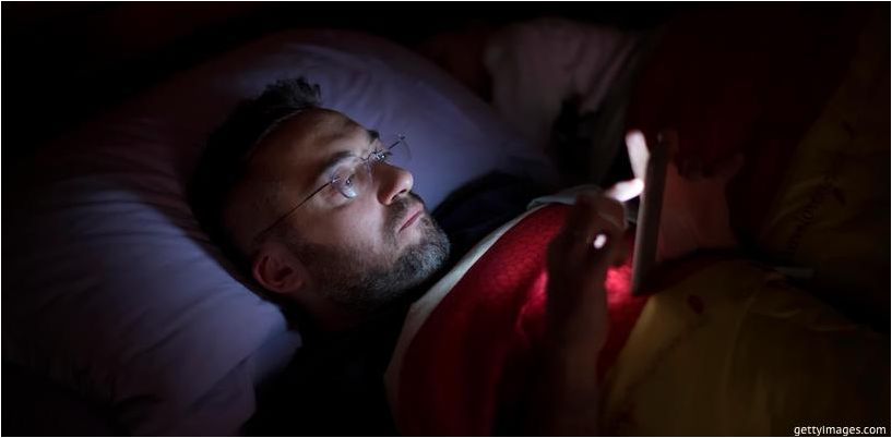 az ember lefeküdve néz a telefonra